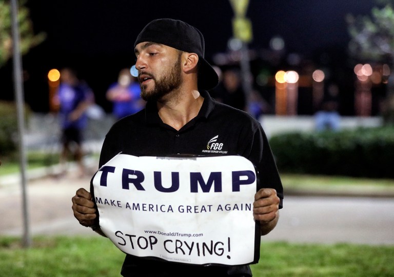 Donald Trump supporter Sergio Fraguela makes a stand as a large crowd protest in opposition of the President-elect. Some of Trump's supporters see themselves as the 'resistance' to the status quo. (Damon Higgins/Palm Beach Post via AP)