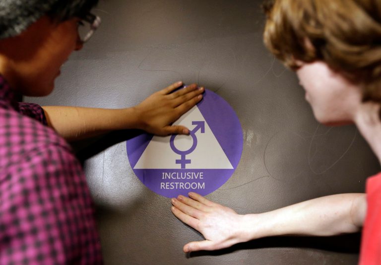 Destin Cramer, left, and Noah Rice place a new sticker on the door at the ceremonial opening of a gender neutral bathroom at Nathan Hale high school on May 17 in Seattle. (AP Photo/Elaine Thompson)