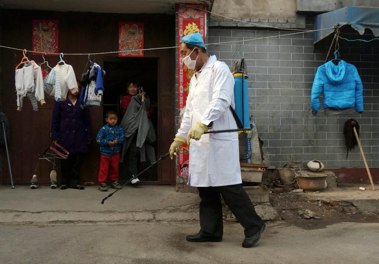 A family watches a worker spray disinfectant in Naidong village, where a boy tested positive for the H7N9 virus, in Beijing Monday, April 15, 2013. The new case of bird flu in China's capital, a 4-year-old boy who displayed no symptoms, is adding to the unknowns about the latest outbreak that has caused 63 confirmed cases and 14 deaths, health officials said Monday. (AP Photo) CHINA OUT