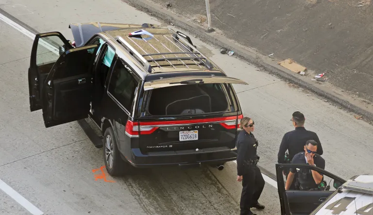 Los Angeles police officers stand at the scene of the end of a pursuit of a hearse with a body inside on Interstate 110 in South Los Angeles Thursday, Feb. 27, 2020, after it was stolen late Wednesday.