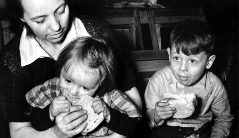 This is an undated photo of a child, hungry after a six-day delay in the issuance of food, biting down on a ham sandwich as he sits down on his mother's lap at a relief station in Cleveland, Ohio, during the Great Depression. 
