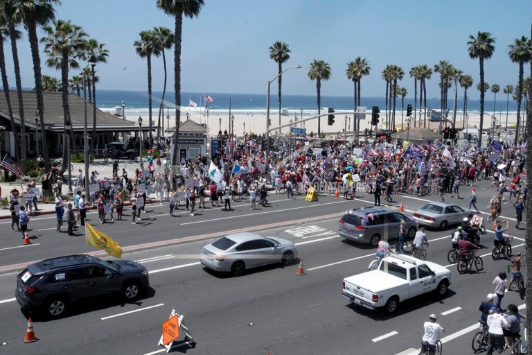Protesters hold signs and wave flags in a demonstration on May Day during the coronavirus pandemic at the pier, Friday, May 1, 2020, in Huntington Beach, Calif. (AP Photo/Chris Carlso)