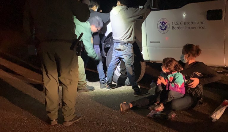 A young girl and her mother watch as two men are patted down for weapons by a Border Patrol agent.