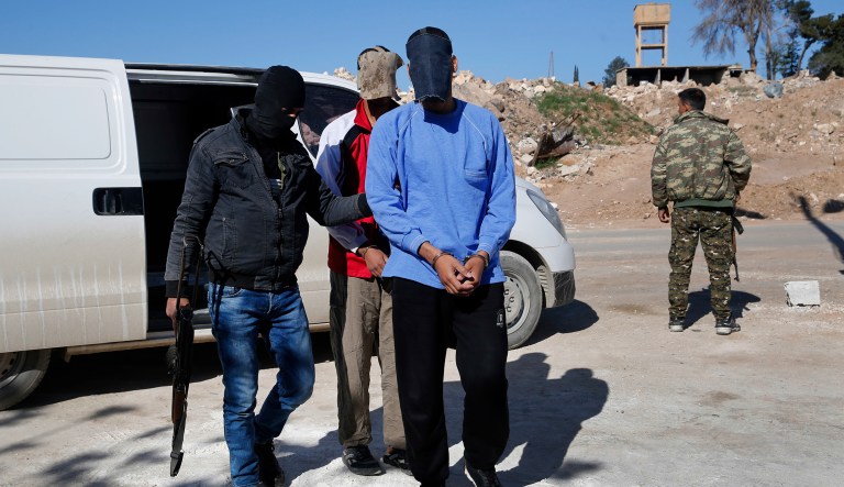 Kurdish security escorts two blindfolded British alleged members of an Islamic State group cell dubbed "The Beatles," known for beheading hostages, Alexanda Amon Kotey, foreground, and El Shafee Elsheikh, background, at a security center, in Kobani, Syria, Friday, March 30, 2018.