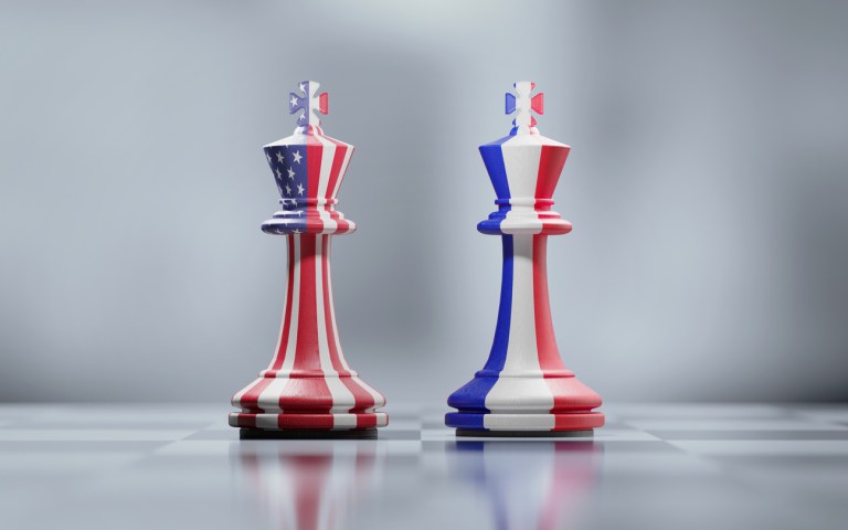Two king chess pieces textured with American and French flags on black and white chessboard. Politics and checkmate concept. Horizontal composition with selective focus and copy space.
