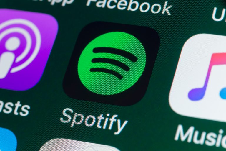 The buttons of the music streaming app Spotify, surrounded by Podcasts, Apple Music, Facebook, and other apps on the screen of an iPhone are shown.