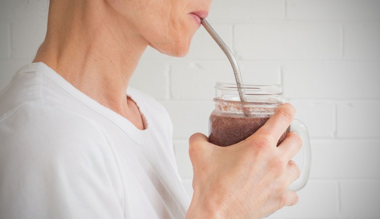 A woman drinks a smoothie from a glass jar using a metal straw.