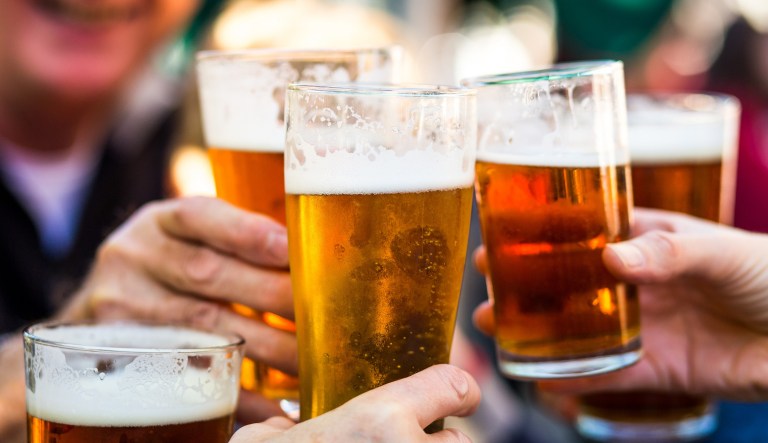 Close-up color image depicting a group of people celebrating with a toast. The people cheers their glasses of beer (pints of beer) together in a gesture of celebration, togetherness, and happiness. The people are defocused in the background, while focus is on the glasses of beer in the foreground. Room for copy space.