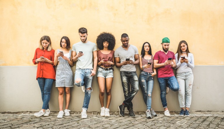 Friends using their cellphones while leaning against a wall.