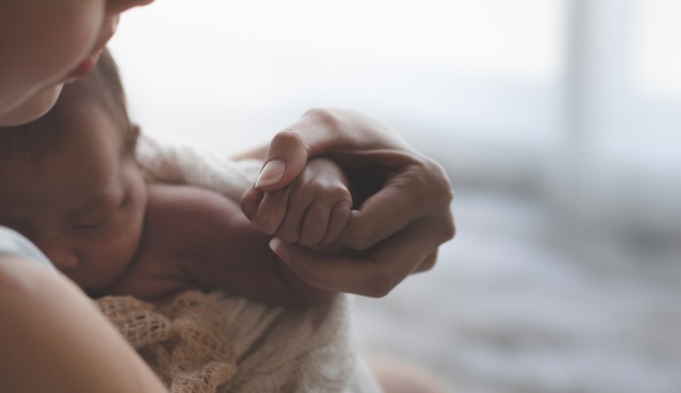 Close-up of a mother holding hands with a newborn baby. 