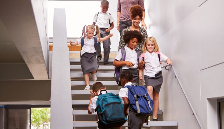 Teacher and pupils walking in busy elementary school corridor.