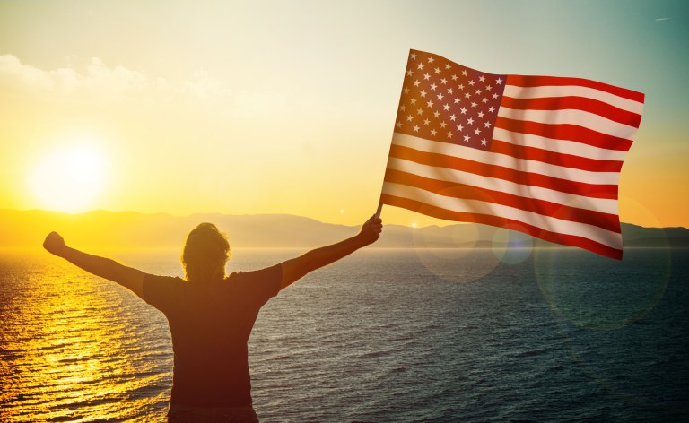 U.S. American flag waving in the wind with beautiful blue sky in background.