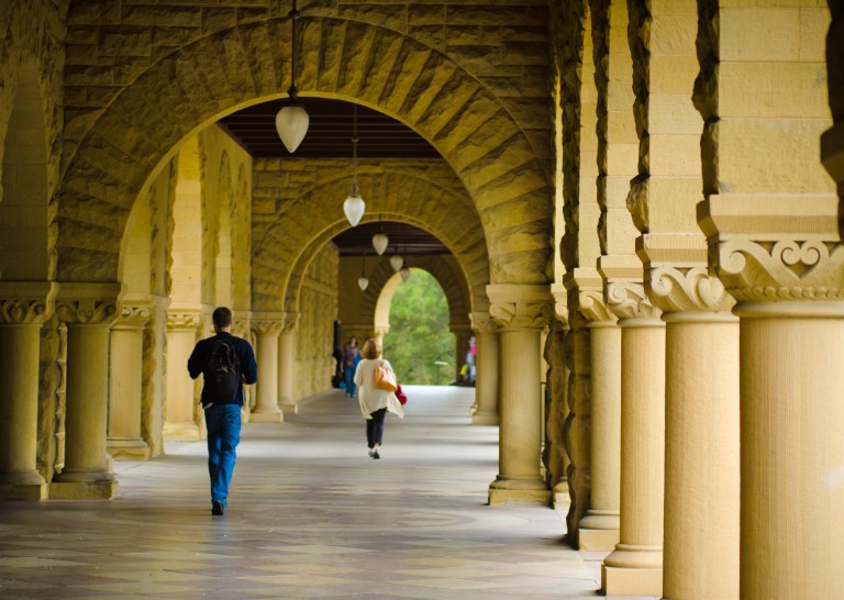 Students walk underneath a covered walkway at the Stanford University campus.