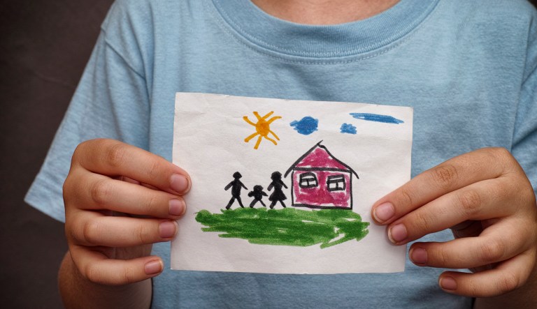 Child holds a drawn house with family.