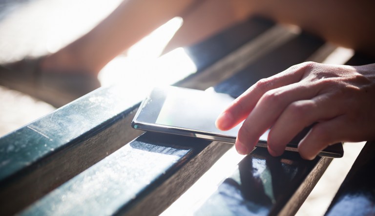 A woman puts down her phone on a bench.