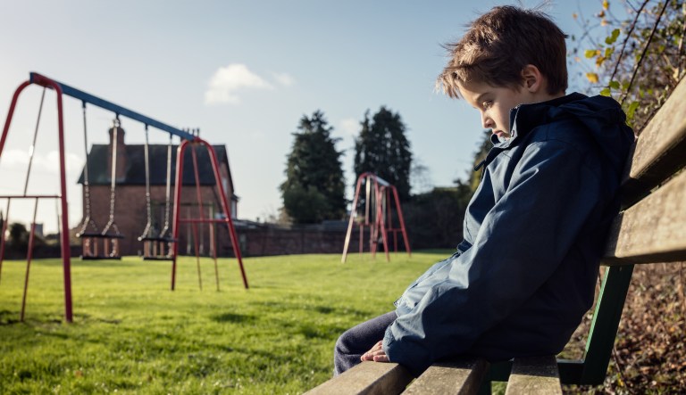 Upset child sitting on play park playground bench concept for bullying, depression, child protection or loneliness.