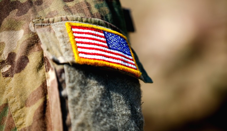 A man is dressed in a military uniform wearing a patch with a U.S. flag.