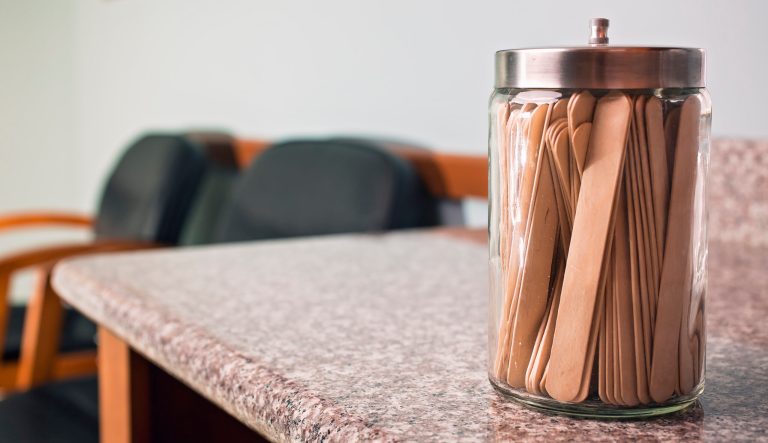A glass container full of tongue depressors in an exam room.