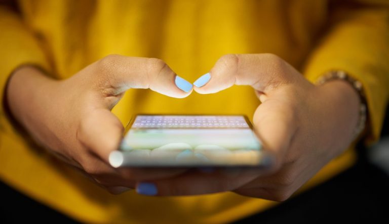 A young woman uses a cellphone to send a text message on a social network at night.