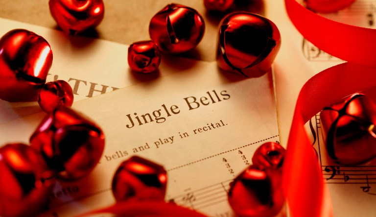 The sheet music of "Jingle Bells", a song that is within the public domain, is surrounded by a curling red ribbon and red Christmas bells of various sizes.