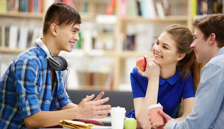 Happy teenagers having snack and talk at break between lessons.