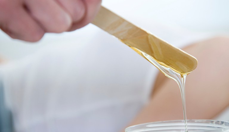 An esthetician at a spa is about to apply some wax on a customer.