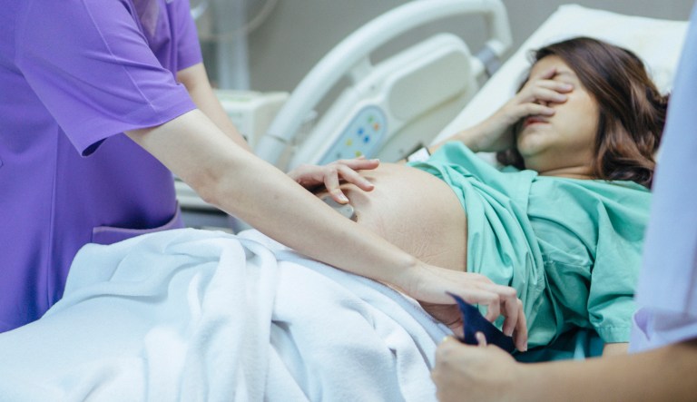 Doctor examining belly of expectant mother in hospital room.