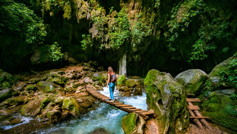 Woman traveling solo crosses wooden bridge at Puente de Dios in San Luis Potosi, Mexico.
