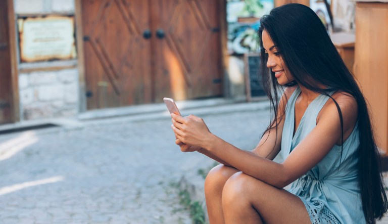 Woman sitting on ground and using smart phone, on street.