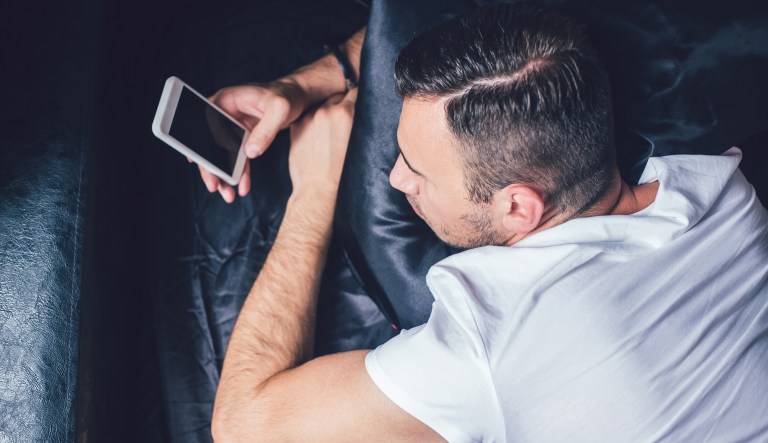 A man using a mobile phone lies in bed.