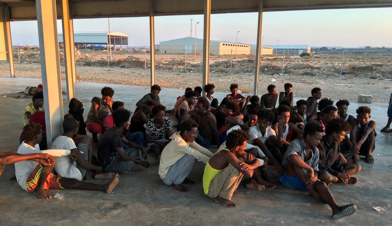 Rescued migrants sit on a coast some 100 kilometers (60 miles) east of Tripoli, Libya, Thursday, July 25, 2019. The U.N. refugee agency and the International Rescue Committee say up to 150 may have perished at sea off the coast of Libya.