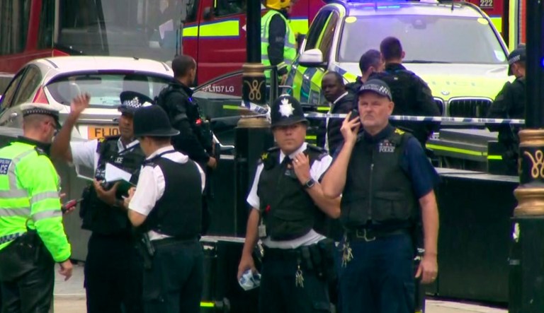 In this frame grab taken Tuesday, Aug. 14, 2018 armed police detain a man, fourth right, who was in a car that crashed into security barriers outside the Houses of Parliament stands to the right of a bus in London. London police say that a car has crashed into barriers outside the Houses of Parliament and that there are a number of injured.