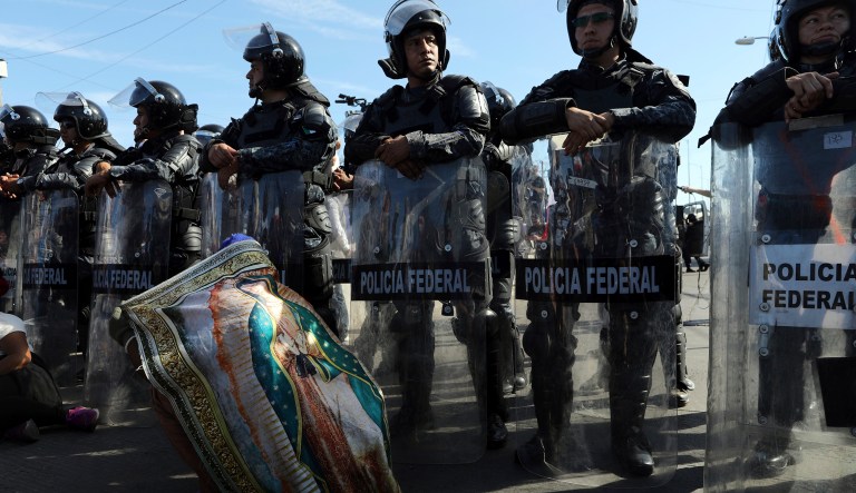 Mexican federal police stand guard over a migrant wearing a Virgen of Guadalupe cloth at the Mexico-U.S. border in Tijuana, Mexico, Sunday, Nov. 25, 2018.