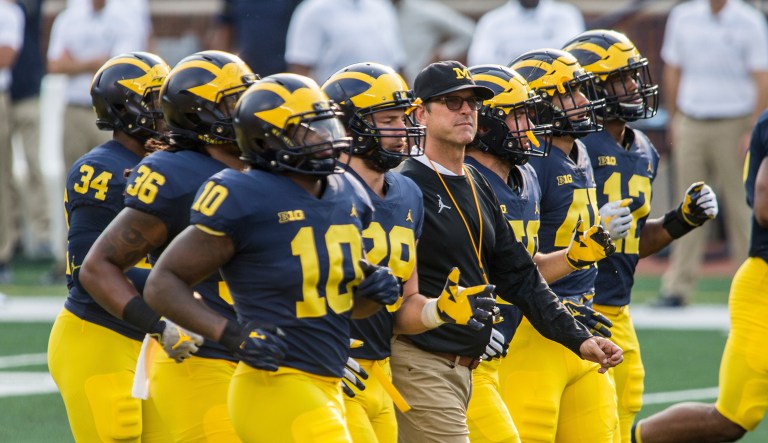 FILE - In this Sunday, Aug. 26, 2018, file photo, Michigan head coach Jim Harbaugh, center, walks the field as players jog around him during an open practice for the NCAA college football team at Michigan Stadium in Ann Arbor, Mich. Michigan plays Notre Dame on Saturday, Sept. 1, to open the college football season.