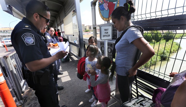 A United States Customs and Border Protection Officer checks the documents of migrants, before being taken to apply for asylum in the United States, on the International Bridge 1 in Nuevo Laredo, Mexico, Wednesday, July 17, 2019.