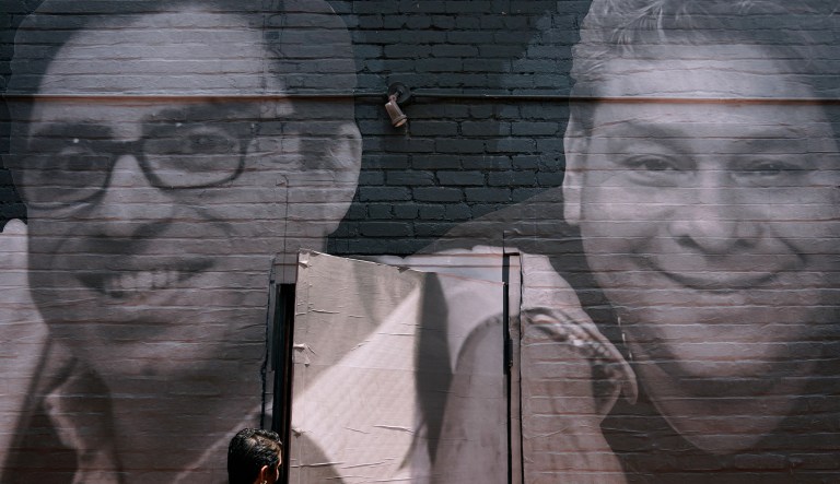 A woman steps through a door that is covered by a mural depicting American hostages and wrongful detainees who are being held abroad, Wednesday, July 20, 2022, in the Georgetown neighborhood of Washington. At left is Siamak Namazi, who has been in captivity in Iran since 2015. At right is Jose Angel Pereira, who has been imprisoned in Venezuela since 2017. 