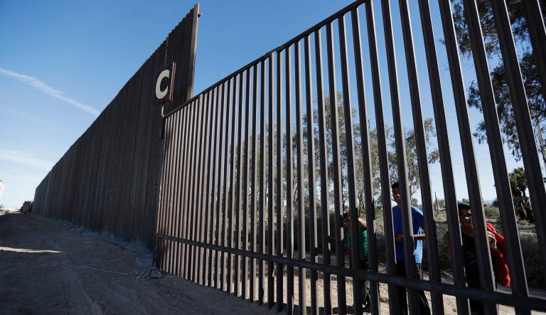 In this March 5, 2018, photo, boys look through an older section of the border structure from Mexicali, Mexico, alongside a newly-constructed, taller section, left, in Calexico, Calif. Congress gave President Donald Trump the $1.6 billion he sought for one year of funding of the border wall with Mexico, but he wanted a long-term wall financing commitment.