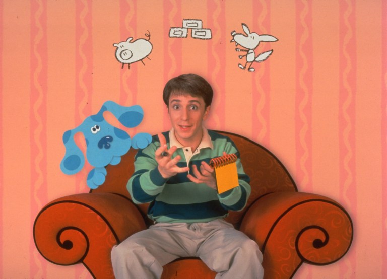 Steve Burns, the main actor in Blue's Clues, sits on a chair as his dog Blue and other animated figures appear behind him.