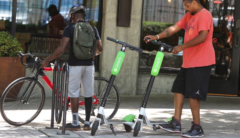 In this Tuesday, June 26, 2018 photo, a man parks his rented dockless scooter outside of a restaurant in Atlanta. 