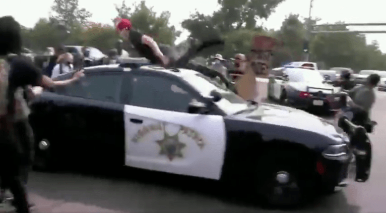 Anti-Trump protester climbs on top of police car and gets thrown off when cruiser speeds up