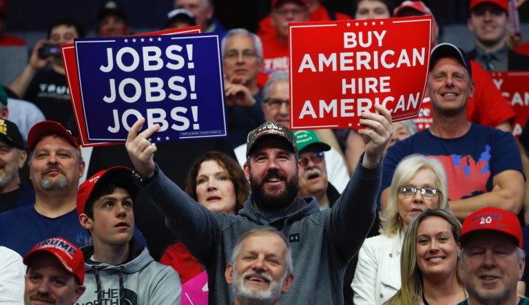 A supporter holds signs for Jobs and Buy American Hire American during a rally for President Donald Trump in Grand Rapids, Mich.