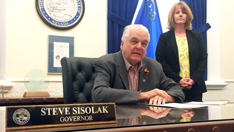 Nevada Gov. Steve Sisolak sits at his desk at the Capitol in Carson City before signing a bill that opens the books on applications for licenses to sell recreational marijuana Friday, May 10, 2019. Melanie Young, executive director of the state Department of Taxation, looks on. 