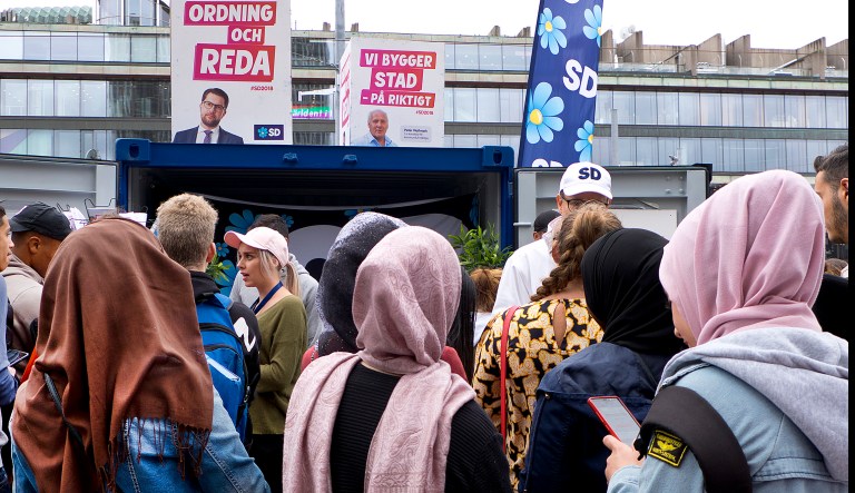 In this Aug. 31, 2018 photo young women listen to a party member of the right wing Sweden Democrats in Stockholm, Sweden.