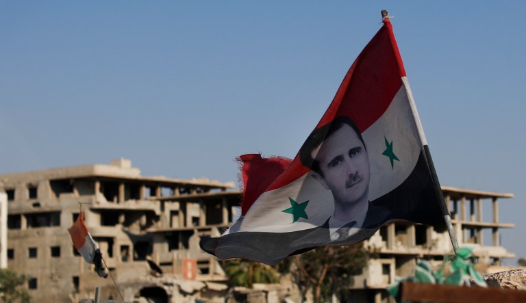 In this Sunday, July 15, 2018, photo, a Syrian national flag with the picture of the Syrian President Bashar Assad hangs at an Army check point in Douma, Syria.