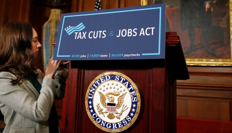 A House staff member affixes a sign that says "Tax Cuts and Jobs Act" ahead of a gathering of House Republicans making statements to the media following a vote on the GOP tax overhaul bill, Thursday, Nov. 16, 2017, on Capitol Hill in Washington.