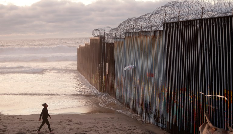 A woman walks on the beach Wednesday, Jan. 9, 2019, next to the border wall topped with razor wire in Tijuana, Mexico.