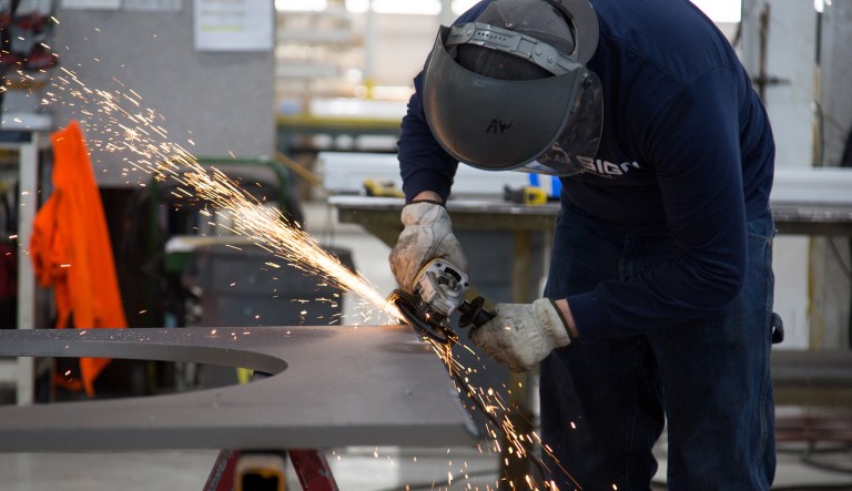 A worker uses an angle grinder while constructing a base plate for a sign pole at the Jones Sign Co. manufacturing facility in De Pere, Wisconsin, U.S., on Monday, Jan. 21, 2019.