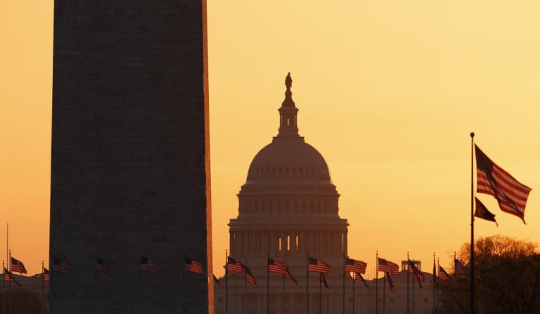 The Capitol Building during a yellow sunrise, with the Washington Monuments pole jutting in the left of the frame.