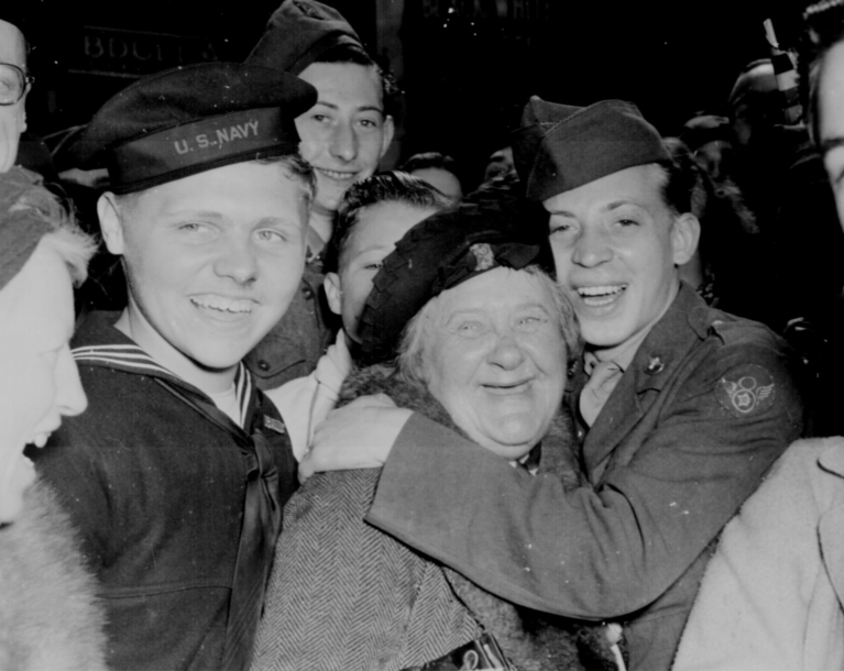 Jubilant American soldier hugs motherly English woman and victory smiles light the faces of happy service men and civilians at Piccadilly Circus, London, celebrating Germany's unconditional surrender." Pfc. Melvin Weiss, England, May 7, 1945