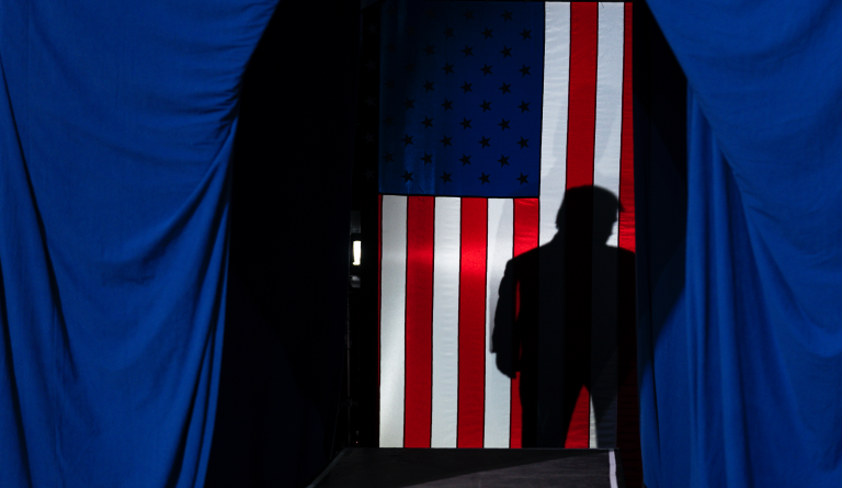 The shadow of President Donald Trump falls on a flag during a campaign rally at The Broadmoor World Arena, Thursday, Feb. 20, 2020, in Colorado Springs, Colo. (AP Photo/Evan Vucci)